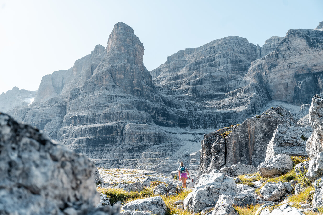 Wanderer geht zwischen Felsen mit hohen Felsbergen im Hintergrund.