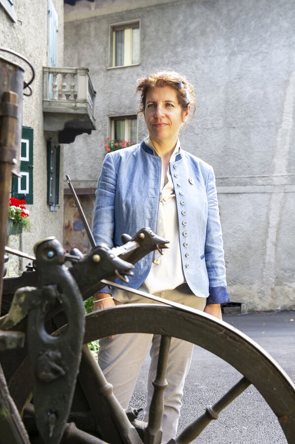 Woman poses with a large metal wheel in a building's courtyard.