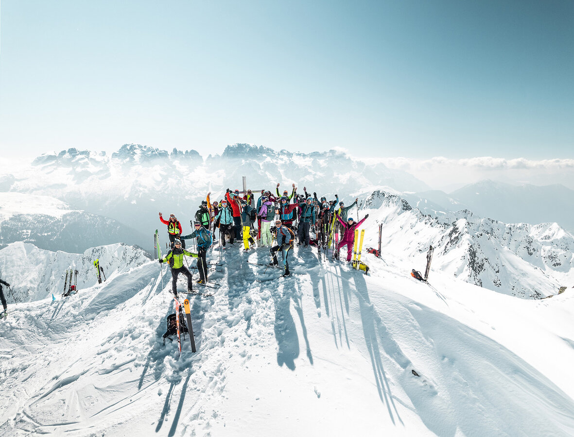 Gruppo di sciatori festeggia sulla cima innevata di una montagna soleggiata.