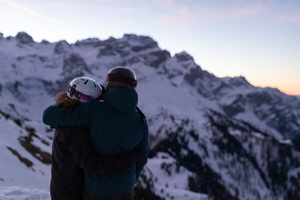 Coppia con caschi da sci abbracciata davanti a montagne innevate al tramonto