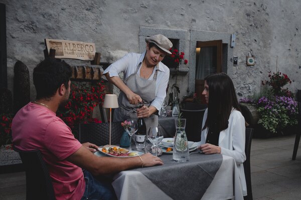 Cameriera serve vino a coppia seduta a tavolo all'aperto di un albergo.