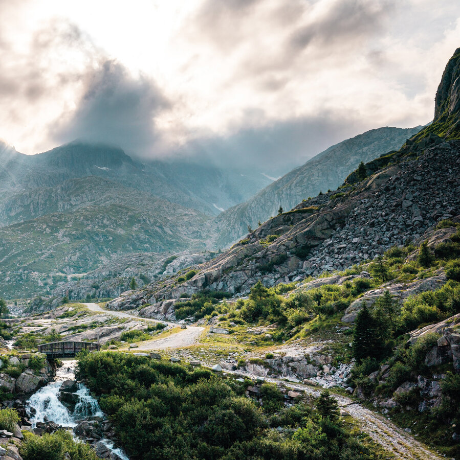 Mountain landscape with path, bridge, and cloudy sky at sunset